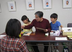 似顔絵を描いている内藤勲さんと覗いている子どもたちです。