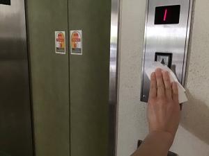 この写真はエレベーターのボタンを消毒しているところです。