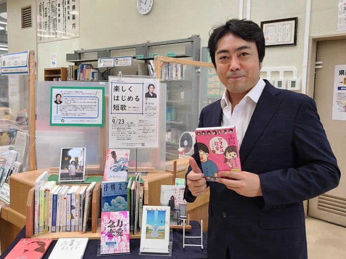 この写真は笹公人先生が図書館でご自分の著書を手ににこやかにポーズしているところです