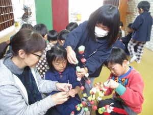 保育士と子どもたちが赤芽の木に団子を飾っている様子