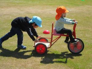 5歳児と3歳児が一緒に三輪車で遊んでいる画像