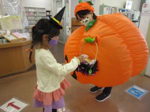 この写真は、子供がハロウィンカボチャの着ぐるみの人から何かをもらっている様子です。