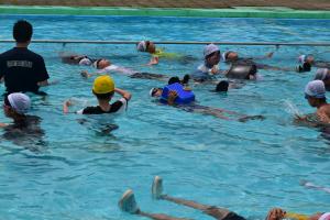 小学生がペットボトルやランドセルなど浮力のあるもので浮く練習をしています