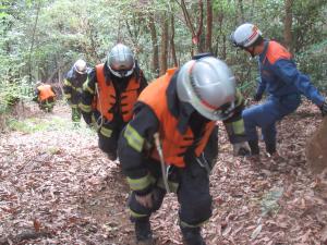 消防隊員が消火水のうを背負い山を登る様子です